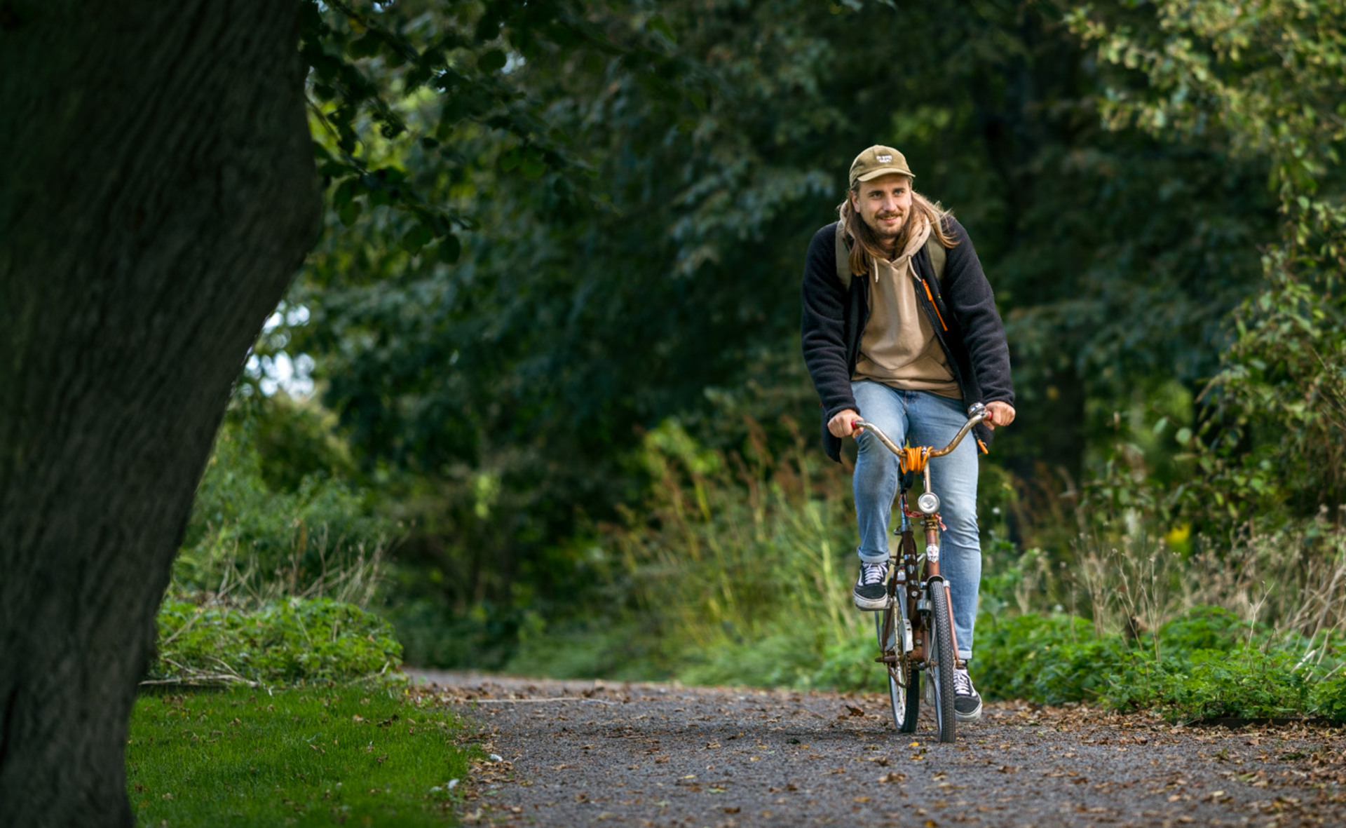 Ung, leende man cyklar i grönskande omgivning i Höganäs
